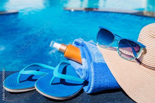 Blue slippers with sunscreen cream, towel, straw hat and sunglas
