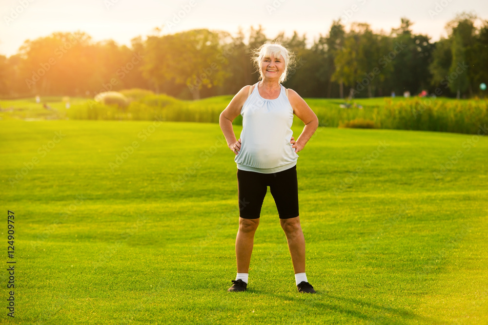 Senior woman standing outdoors. Smiling lady on grass background. I train every morning. Save health through years. Senior woman standing outdoors. Smiling lady on grass background. I train every morning. Save health through years.