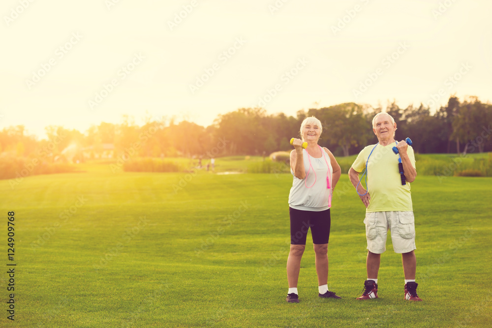 Couple with dumbbells smiling. Senior people standing outdoor. New training program for pensioners. Life and sports. Couple with dumbbells smiling. Senior people standing outdoor. New training program for pensioners. Life and sports.