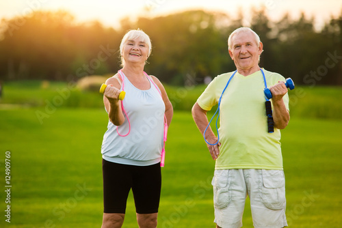 Fototapeta Naklejka Na Ścianę i Meble -  Elderly couple with dumbbells. People doing exercise and smiling. Sportsmen never get old. Mood and motivation.