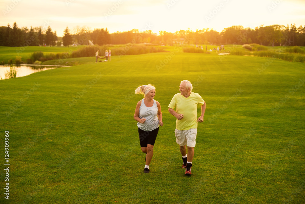 Elderly couple is jogging. Smiling people on meadow. Be in motion. The lightness of moves. Elderly couple is jogging. Smiling people on meadow. Be in motion. The lightness of moves.