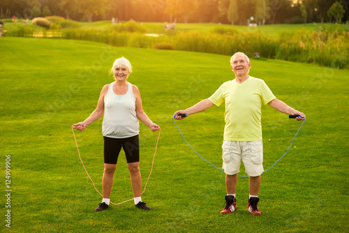 Couple with skipping ropes outdoor. Smiling elderly woman and man. Health of lungs and heart. Count your jumps.