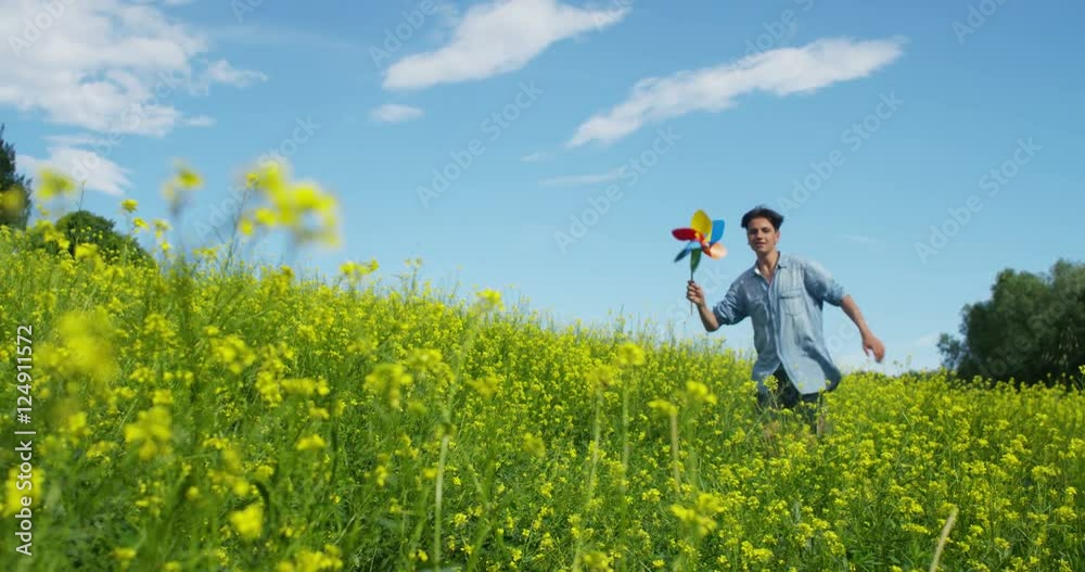  in a day of sun and wind, a happy nice beautiful boy in green nature blows on a colorful pinwheel helped by the energy of fresh wind . concept of happiness and renewable wind energy.6k resolution