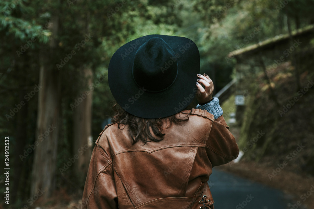 girl with hat walking along the road behind the forest