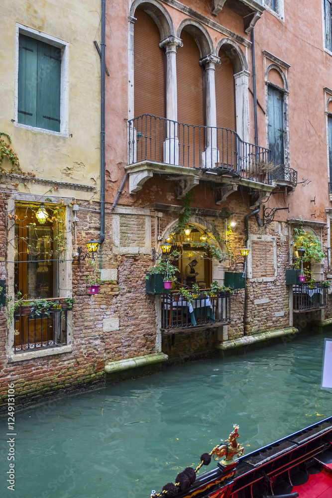 Narrow venetian canal among colorful brick houses in Venice and Traditional Venetian gondola, Italy.