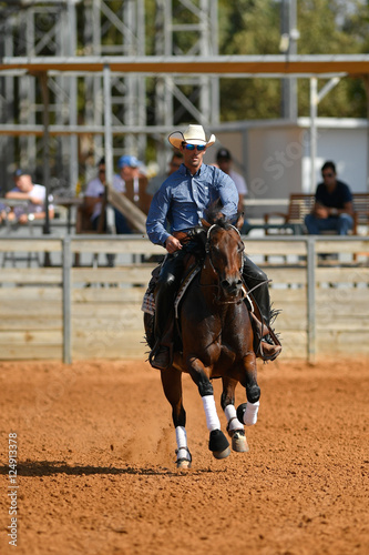 The front view of a rider in cowboy chaps, boots and hat on a horseback performs an exercise during a competition © PROMA