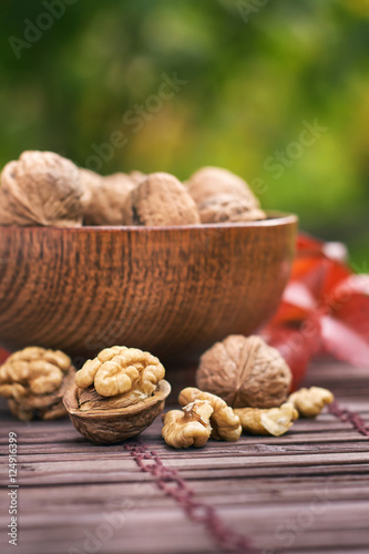 Walnuts in wooden bowl, green blurry background with plenty of copy space.
