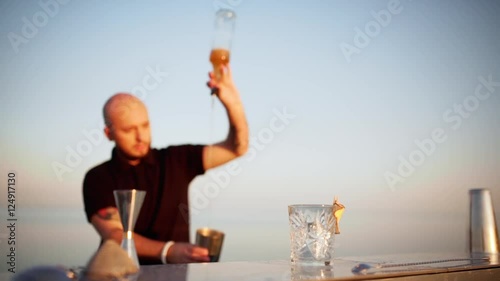 Young handsome bartender preparing cocktail in shaker at seaside Slow motion
