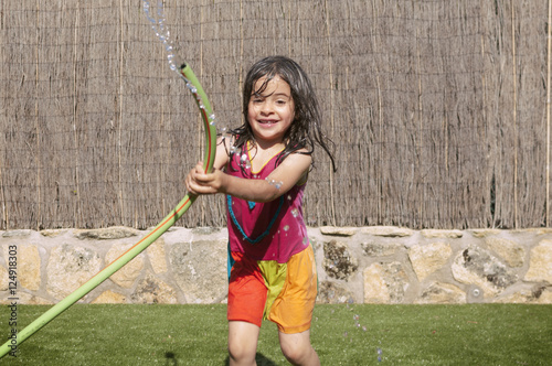Girl playing in the garden getting wet with the hose