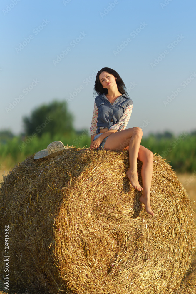 Girl in shorts sitting on a stack of straw