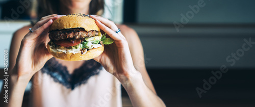 Young girl holding in female hands fast food burger, american unhealthy calories meal on background, mockup with copy space for text message or design, hungry human with grilled hamburger front view