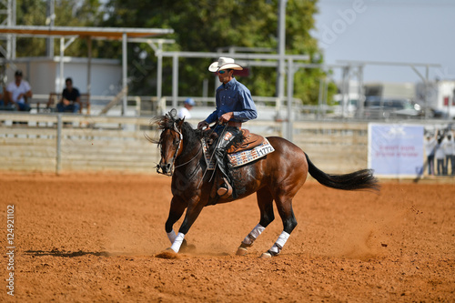 The side view of a rider in cowboy chaps, boots and hat on a horseback performs an exercise during a competition © PROMA