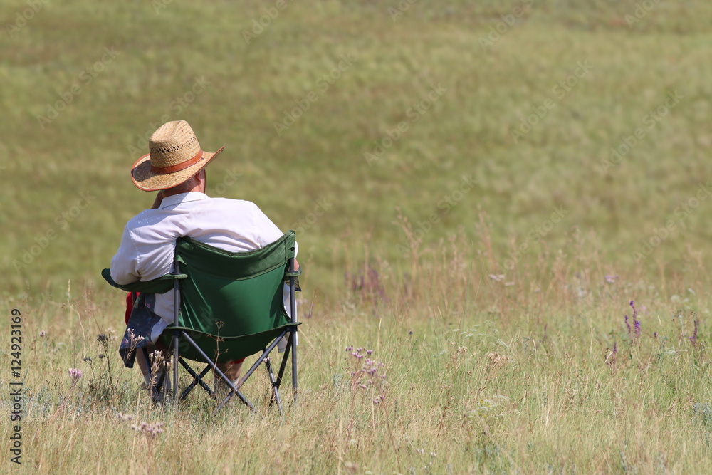 Middle-aged man in a cowboy hat and white shirt sitting in a folding chair, enjoying the steppe freedom Middle-aged man in a cowboy hat and white shirt sitting in a folding chair, enjoying the steppe freedom