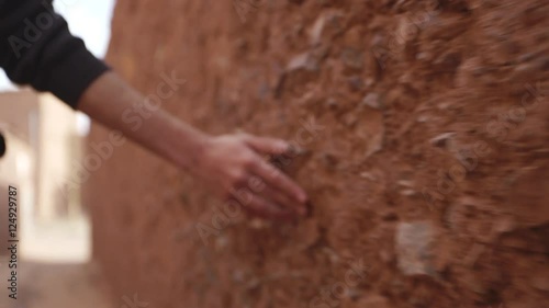 Man walks and grazes hand on stone wall, Morocco.