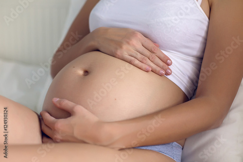 pregnant woman lying in white bed and a white t-shirt stroking belly