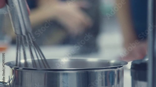Metal pot on the stove. Whisk for stirring. The chef mixes the contents of the pan rim. Cooking of restaurant dishes. The hostess prepares a dish.