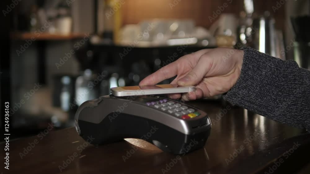 Customer paying with NFC technology by mobile phone on terminal in modern cafe Customer paying with NFC technology by mobile phone on terminal in modern cafe