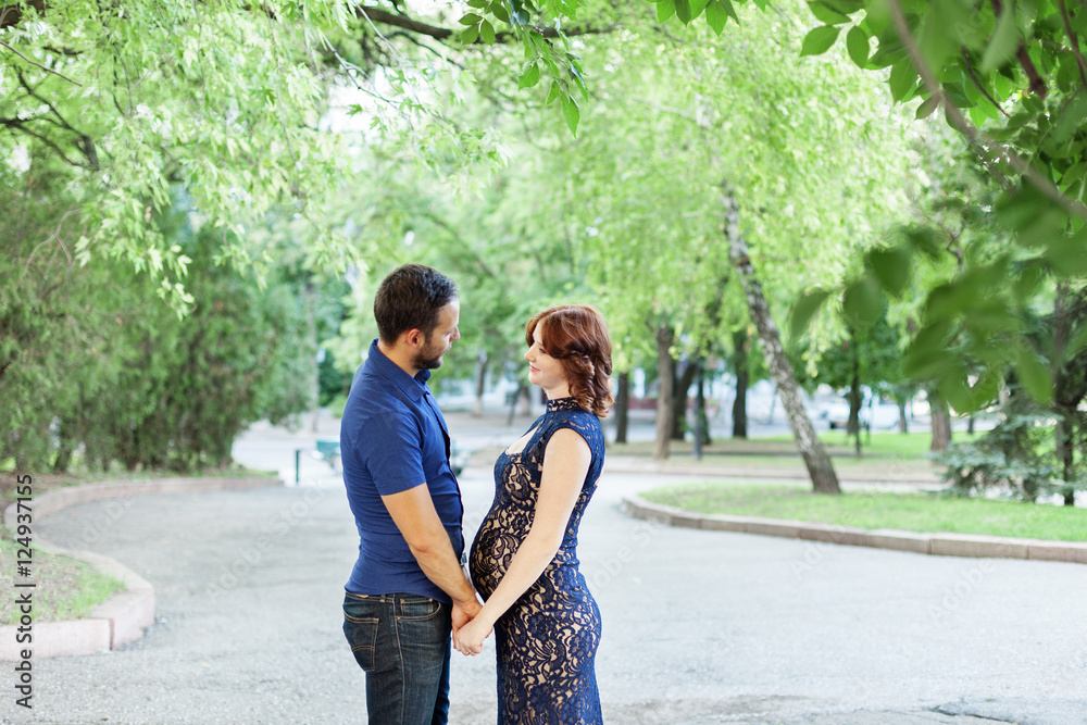 Fototapeta premium Happy pregnant woman with husband standing together in foliage.