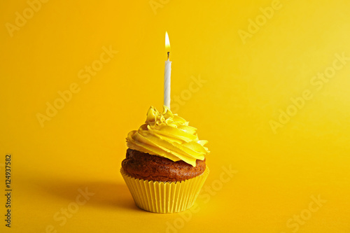 Fresh tasty cupcake with candle on yellow background