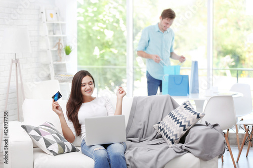 Young woman with laptop shopping online and man on background