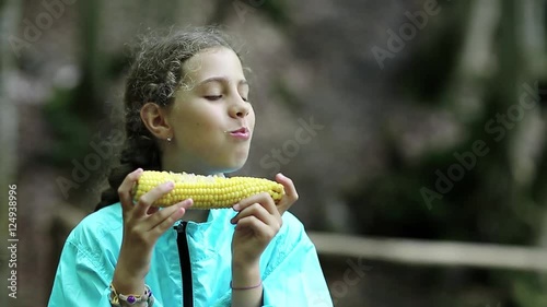 Girl eats corn. Female with corncob. Beautiful girl in blue jacket eats corn and looks around