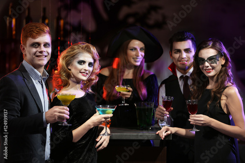 Young people in different costumes drinking cocktails at Halloween party