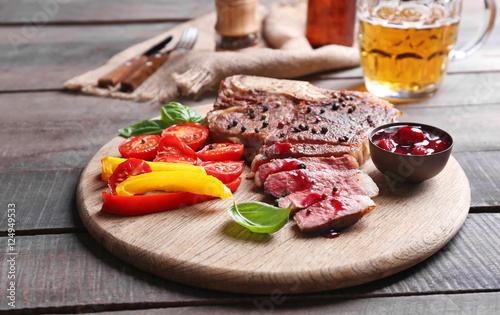 Grilled steak with fresh vegetables, sauce and beer on wooden table