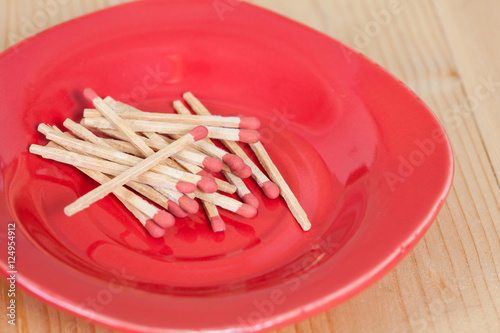 Matchsticks in red plate over wooden background