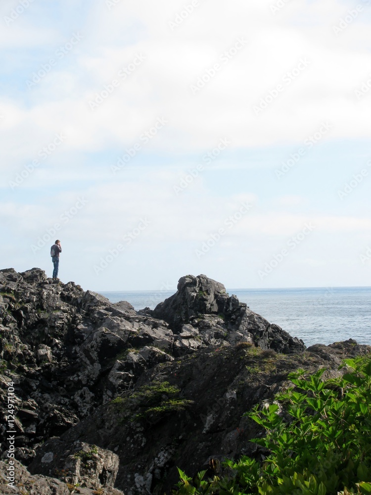 Man traveller talking on mobile phone while standing on a rock near ocean. Vancouver Island, Canada Man traveller talking on mobile phone while standing on a rock near ocean. Vancouver Island, Canada