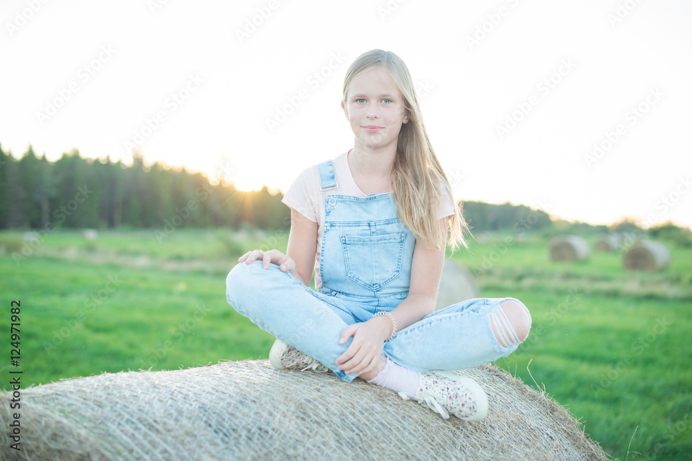 Fototapeta premium Beautiful young girl sitting on the haystack