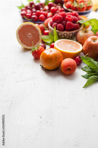 Summer fruits and berries (strawberries, cherries, raspberries, oranges, persimmon) on a white table, space for text, selective focus