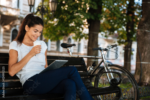Woman with cup of coffee and using tablet outdoors