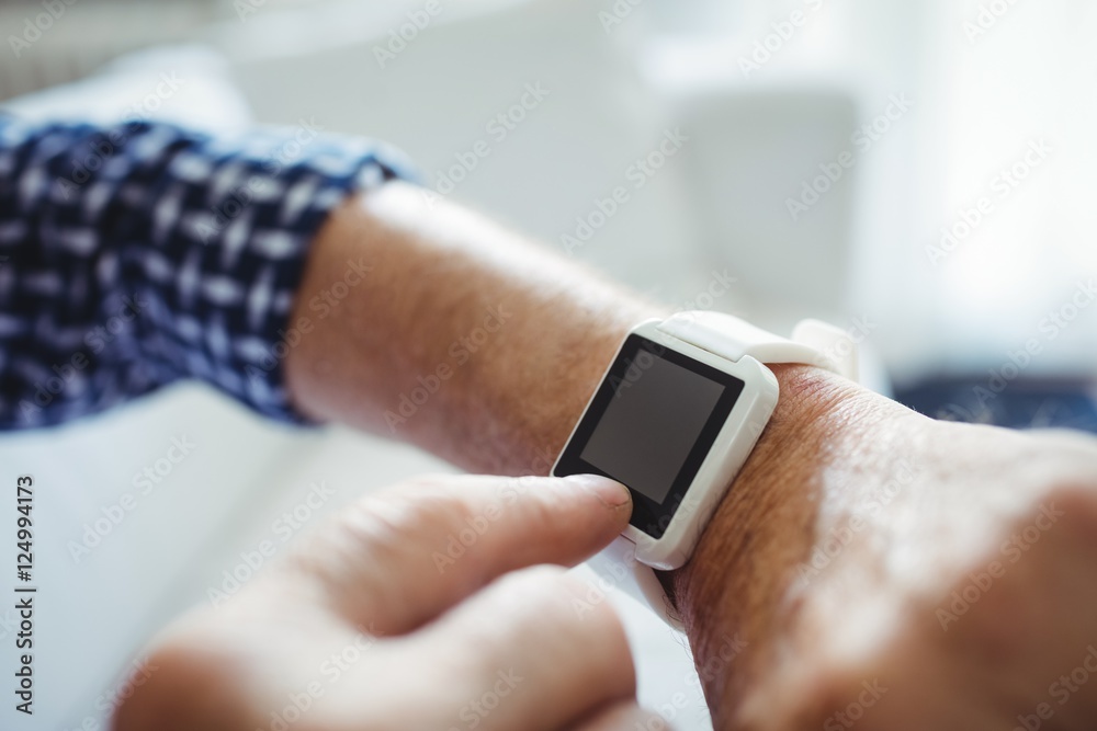 Senior man adjusting a time on smartwatch in living room Senior man adjusting a time on smartwatch in living room