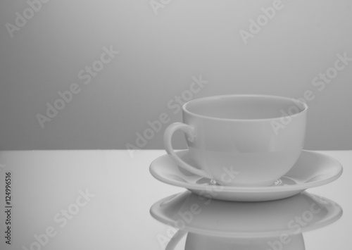 one white cup and saucer on a light background with reflection
