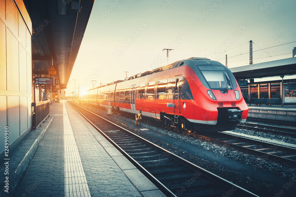 Obraz premium Piękna stacja kolejowa z nowoczesnym wysokiej prędkości czerwony pociąg podmiejski na kolorowy zachód słońca. Linia kolejowa z rocznika tonowaniem. Pociąg na peronie kolejowym. Koncepcja przemysłowa. Turystyka kolejowa