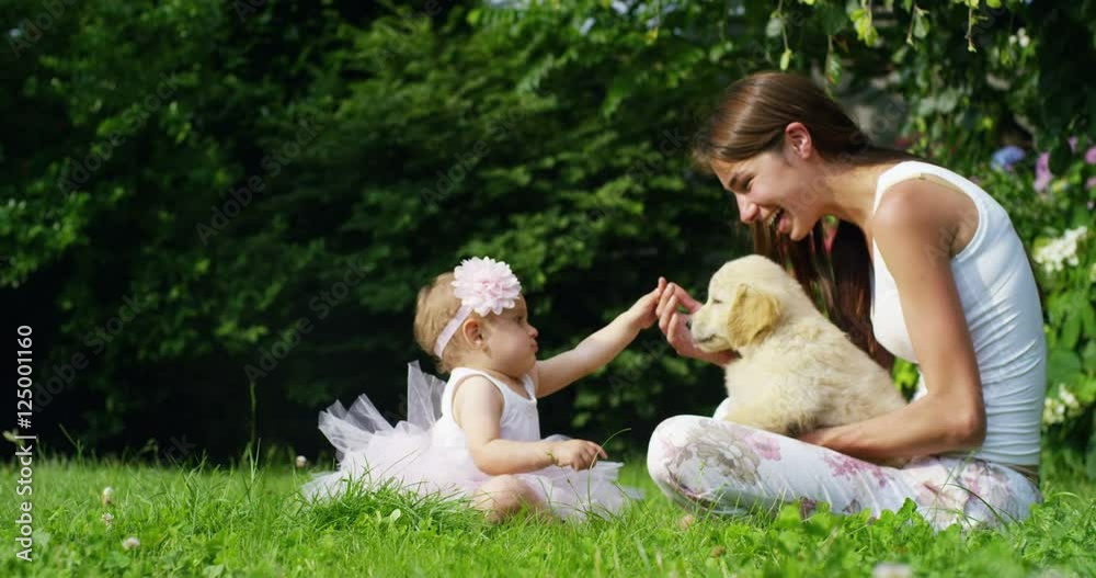 On a sunny spring day a little girl dressed as a ballerina plays with her mom and Golden Retriever puppy in the garden and everyone smiles like a happy family On a sunny spring day a little girl dressed as a ballerina plays with her mom and Golden Retriever puppy in the garden and everyone smiles like a happy family