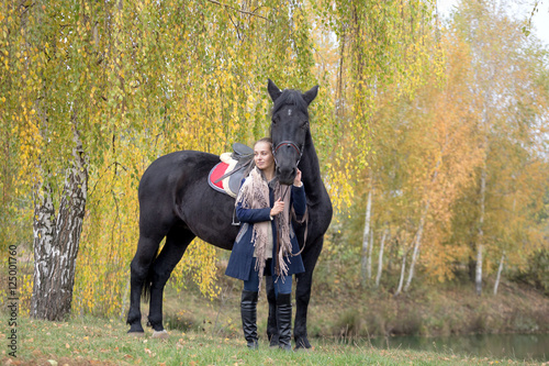 girl with a black horse in the autumn under birch