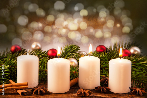 drei brennende Advent-Kerzen vor Weihnachtsschmuck im Tannenzweig