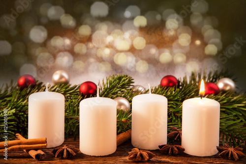 eine brennend Advent-Kerze vor Weihnachtsschmuck im Tannenzweig