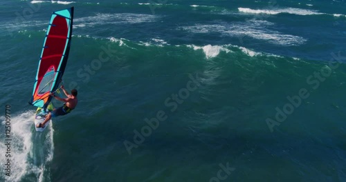Aerial view of windsurfer gliding across blue ocean jumping off wave, extreme sport