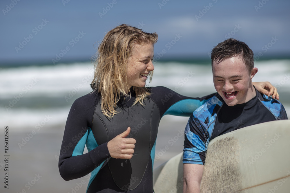 Happy teenage boy with down syndrome and woman with surfboard on beach Happy teenage boy with down syndrome and woman with surfboard on beach