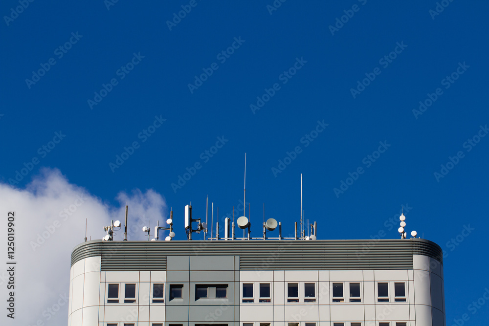 The roof of a tall skyscraper or block of flats with lots of aerials, satellite dishes and communication equipment attached. - obrazy, fototapety, plakaty 