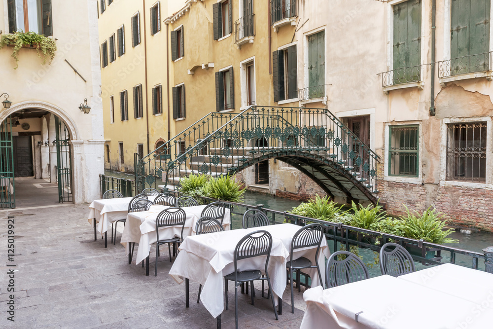 Empty restaurant near the canal in Venice (Italy). The old bridge with cast-iron railing is in the background.