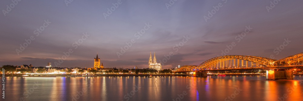 Illuminated Cologne Cathedral and bridge at night in Cologne, panoramic view