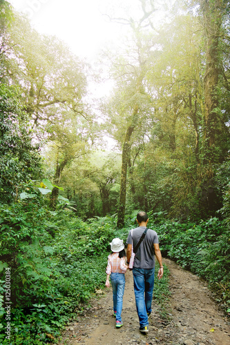 Father and daughter hand in hand walking during the hiking activities in rain forest with sunlight. Fathers day concept, Phuphangmar, phuhin rongkla national park, Petchabun, Thailand.