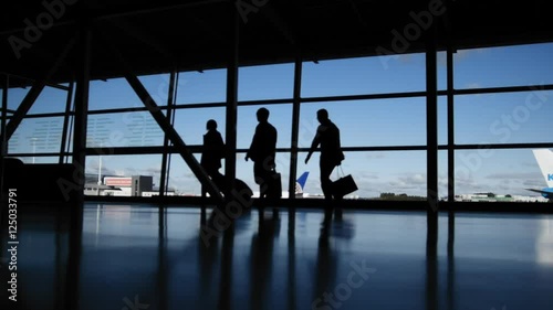 Travellers with suitcases and baggage in airport walking to departures in front of window, silhouette photo