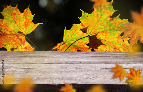 empty wooden board with beautiful autumn leaves on natural blur background.