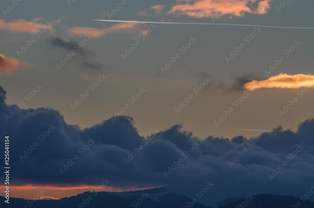 Jet plane flying in the mountains above the clouds at sunset.