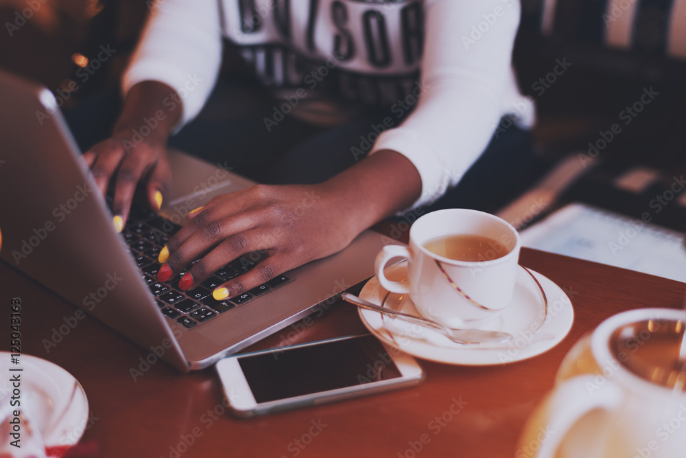 Black hands with .varicoloured nails on laptop keyboard in cafe