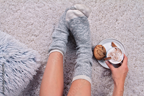 фотографія Woman wearing cozy warm wool socks relaxing at home, drinking cacao, winter lazy day concept, top view